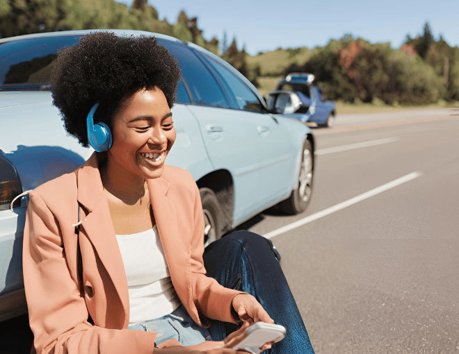 A person sitting in their car on the side of the road, smiling while listening to music on their phone, waiting for a tow truck.